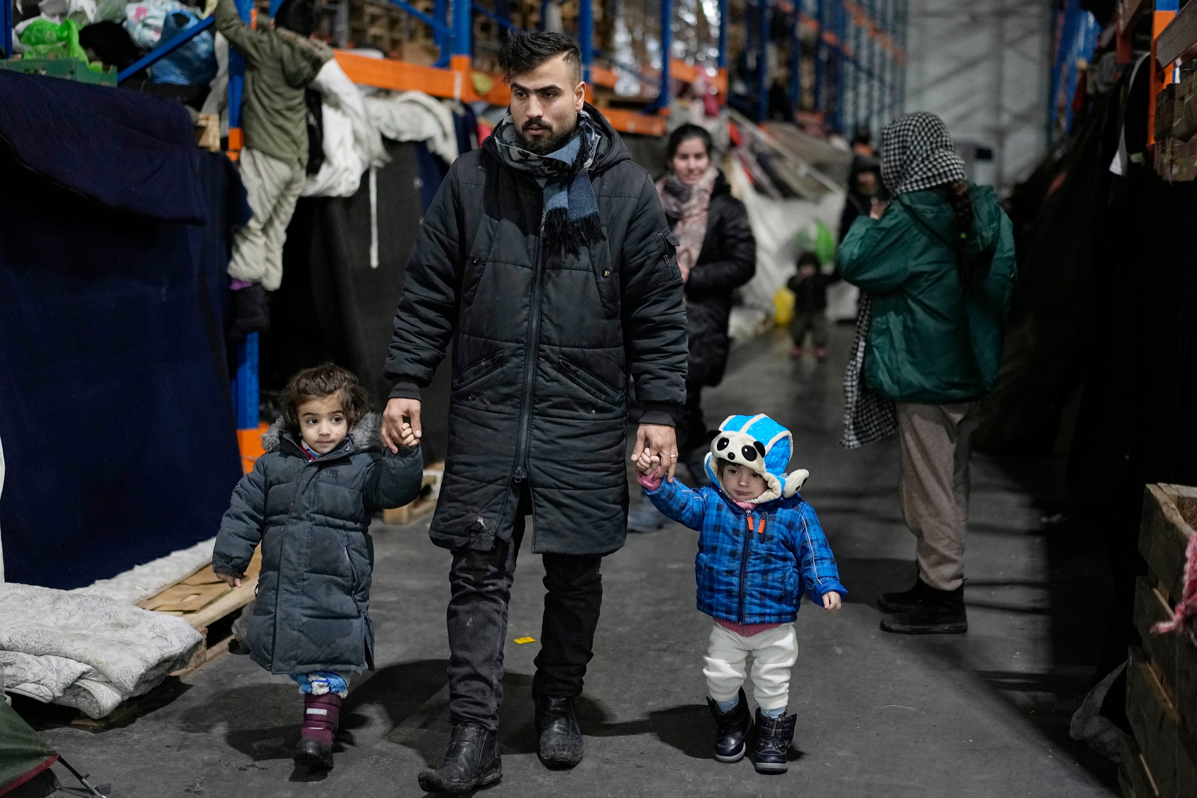 A man walks with his children as migrants settle at the checkpoint logistics center "Bruzgi" at the Belarus-Poland border near Grodno, Belarus, Thursday, Dec. 23, 2021. (AP Photo/Pavel Golovkin)